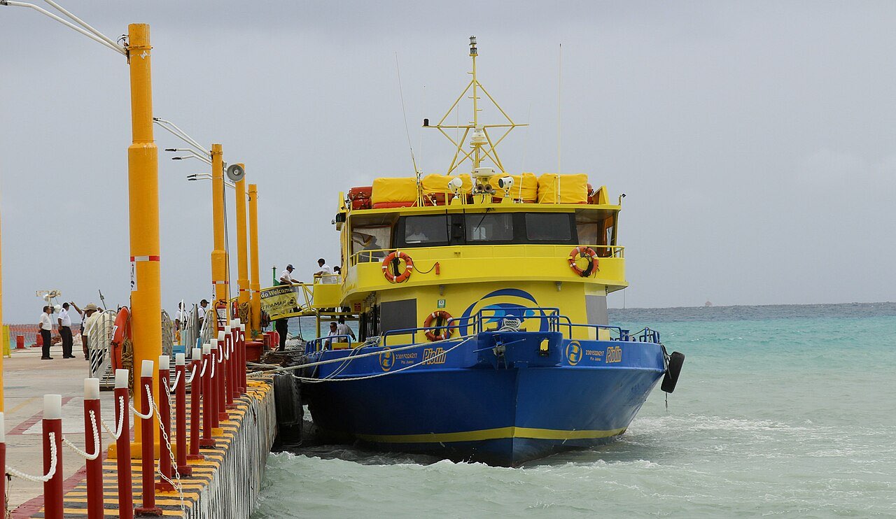 A yellow and blue Ultramar ferry moored alongside a pier on the Caribbean coast