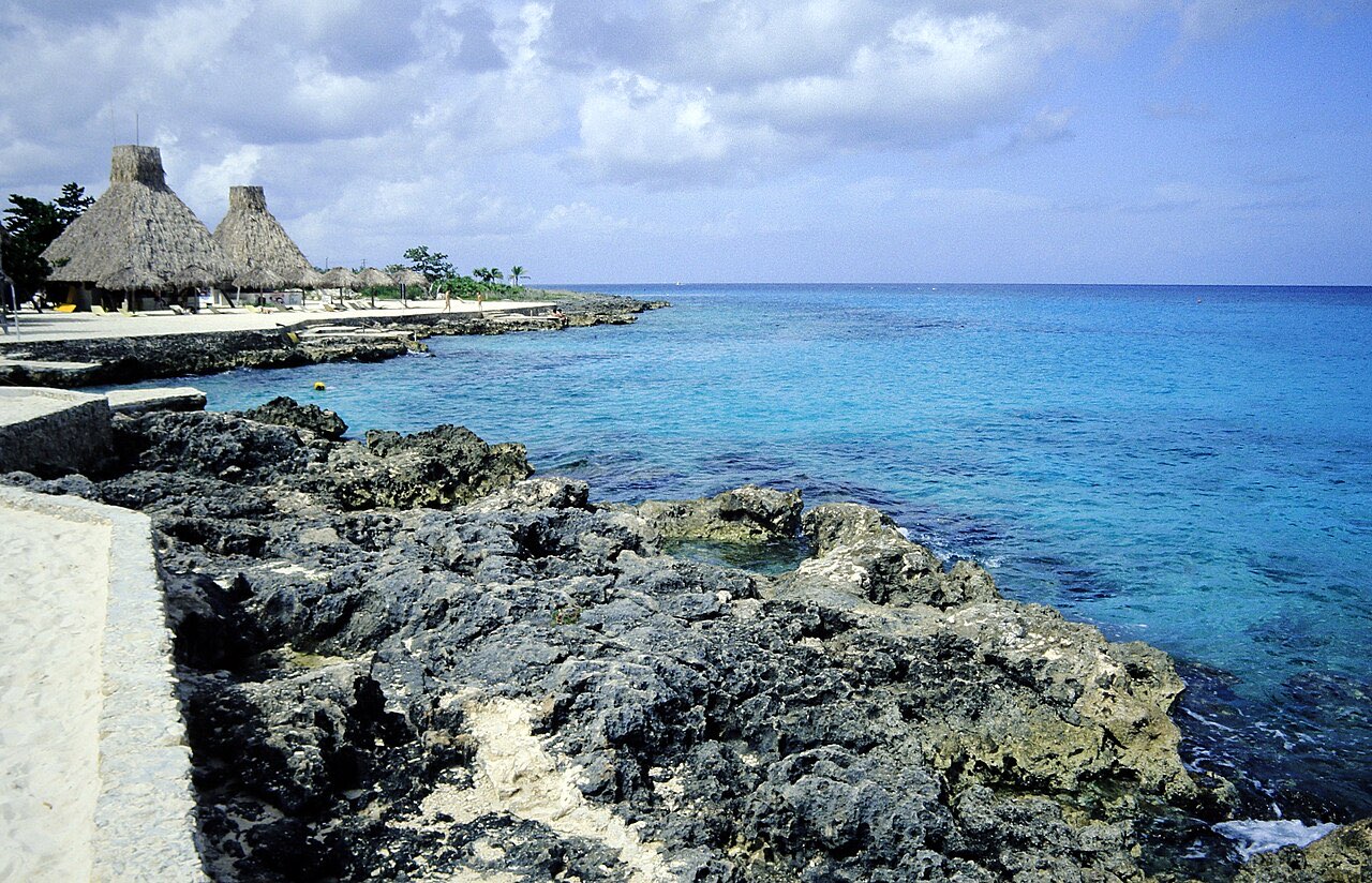Rocky Caribbean shoreline with clear blue water and thatched palapa huts at Chankanaab, Cozumel